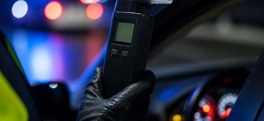 Алкотестер в руке инспектора у автомобиля в ночное время